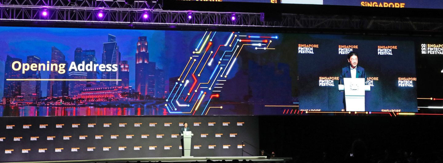 "Singapore Fintech Festival" stage with speaker, large screen featuring "Opening Address" text and city skyline.